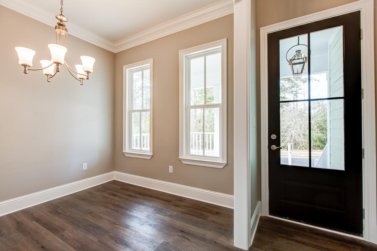 Interior view of a room with dark wood flooring, two double-hung windows, and a black front door with glass panes.