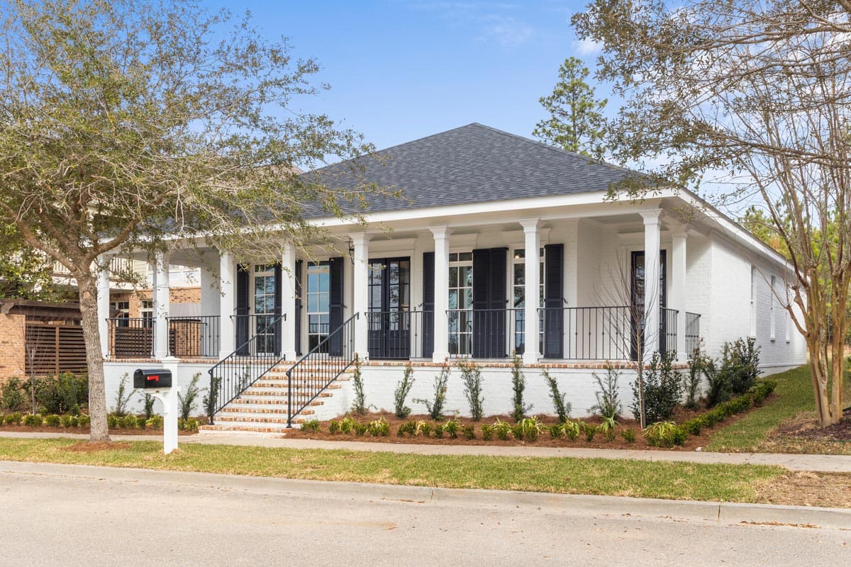 House plan exterior. One-story design with front porch supported by columns. Features include black shutters and a gabled roofline.
