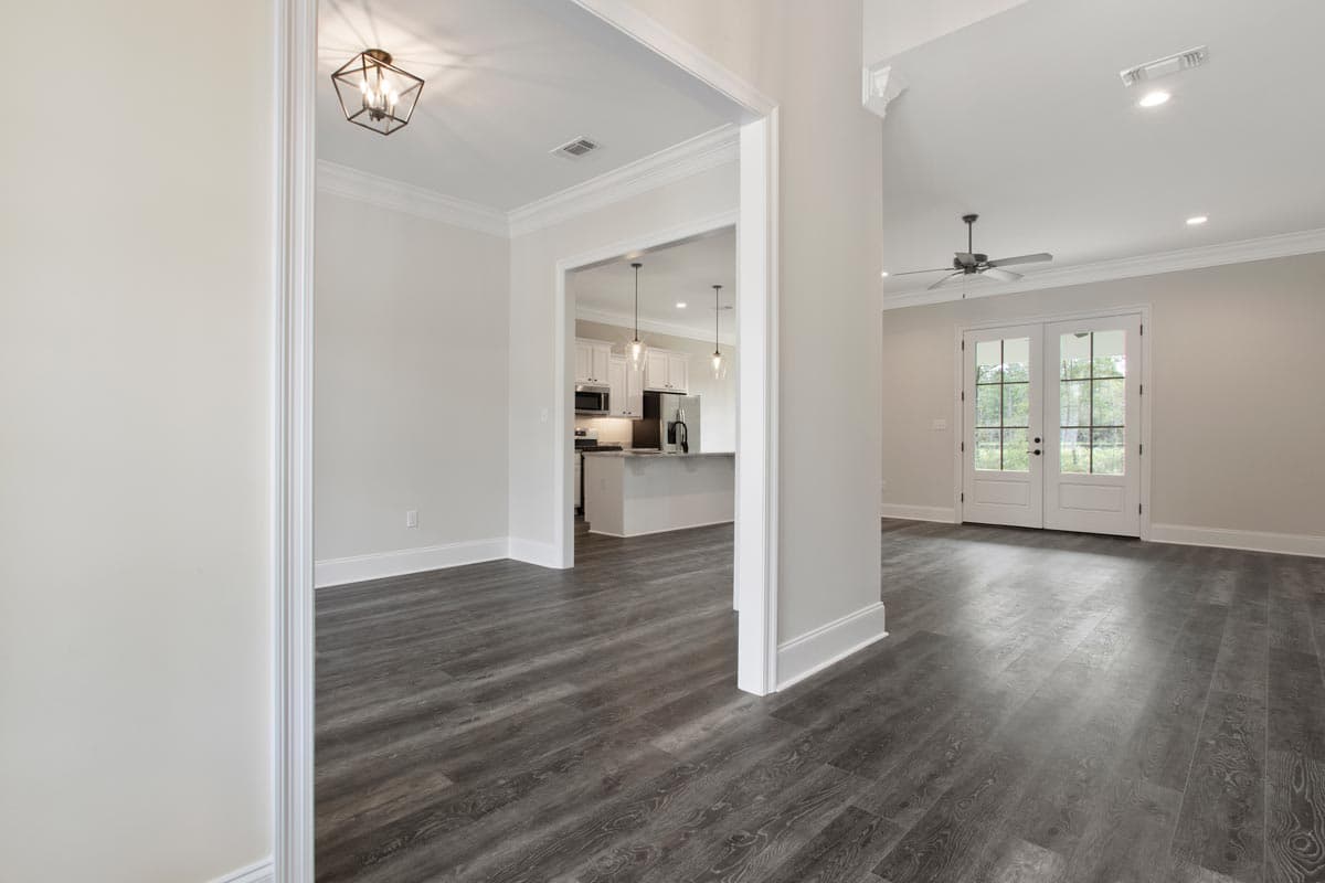 Interior view shows an open living space with a view into a kitchen, featuring double doors and a ceiling fan.