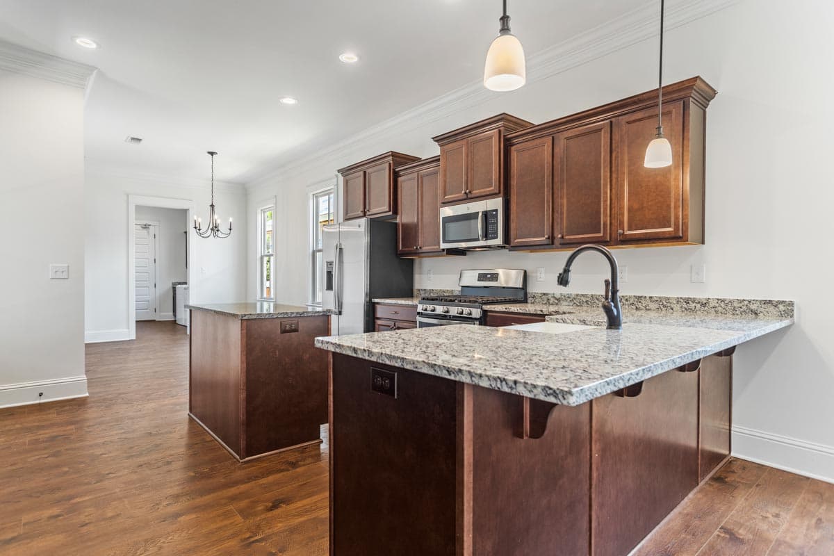 Interior view of a kitchen with two islands, dark wood cabinets, granite countertops, stainless steel appliances, and pendant lights.