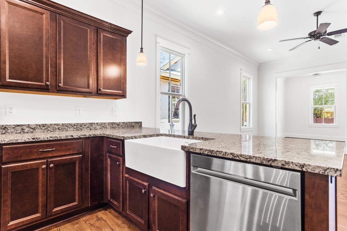 Kitchen with dark wood cabinets, granite countertops, apron sink, stainless steel dishwasher, and pendant lighting.