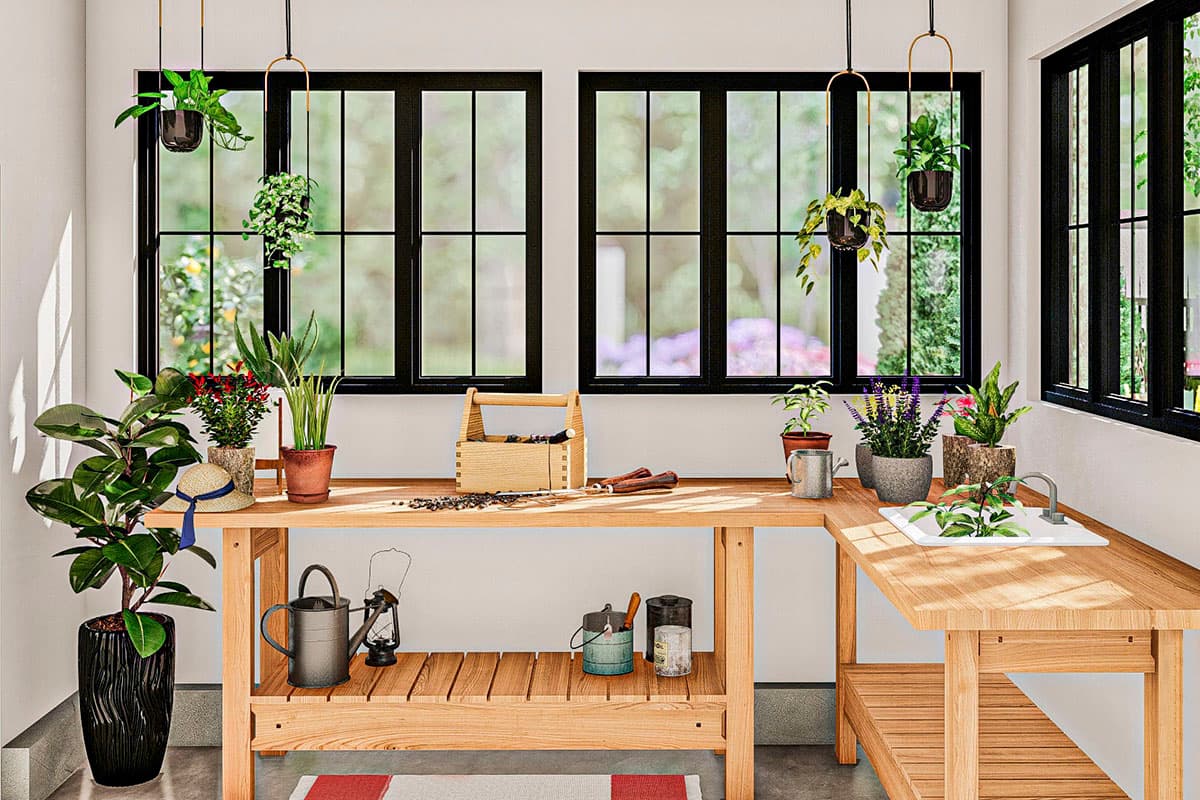 Sunroom with wooden workbench, sink, hanging plants, and large windows with black frames.