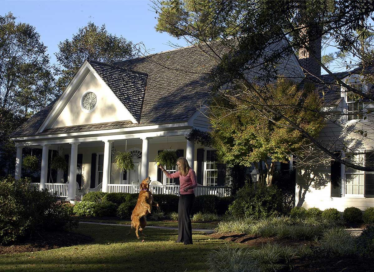 House plan exterior showing a two-story home with a wide wrap-around porch, gabled roof, and circular attic window.