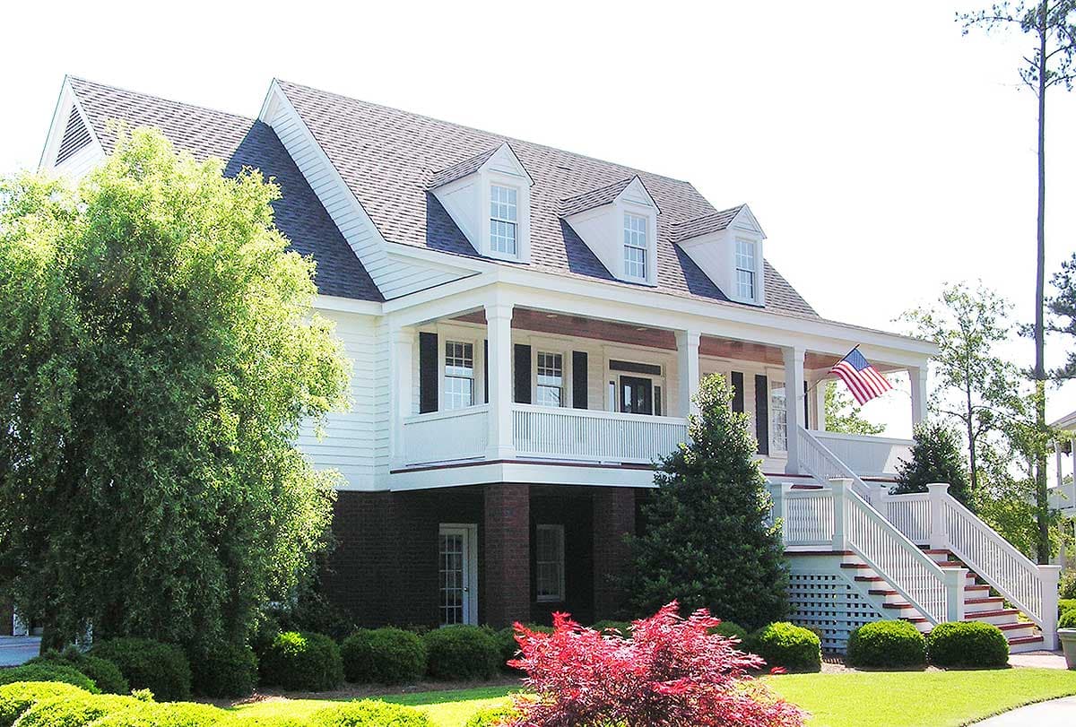 House plan exterior: Two-story home with a wraparound porch, dormer windows, and brick foundation.