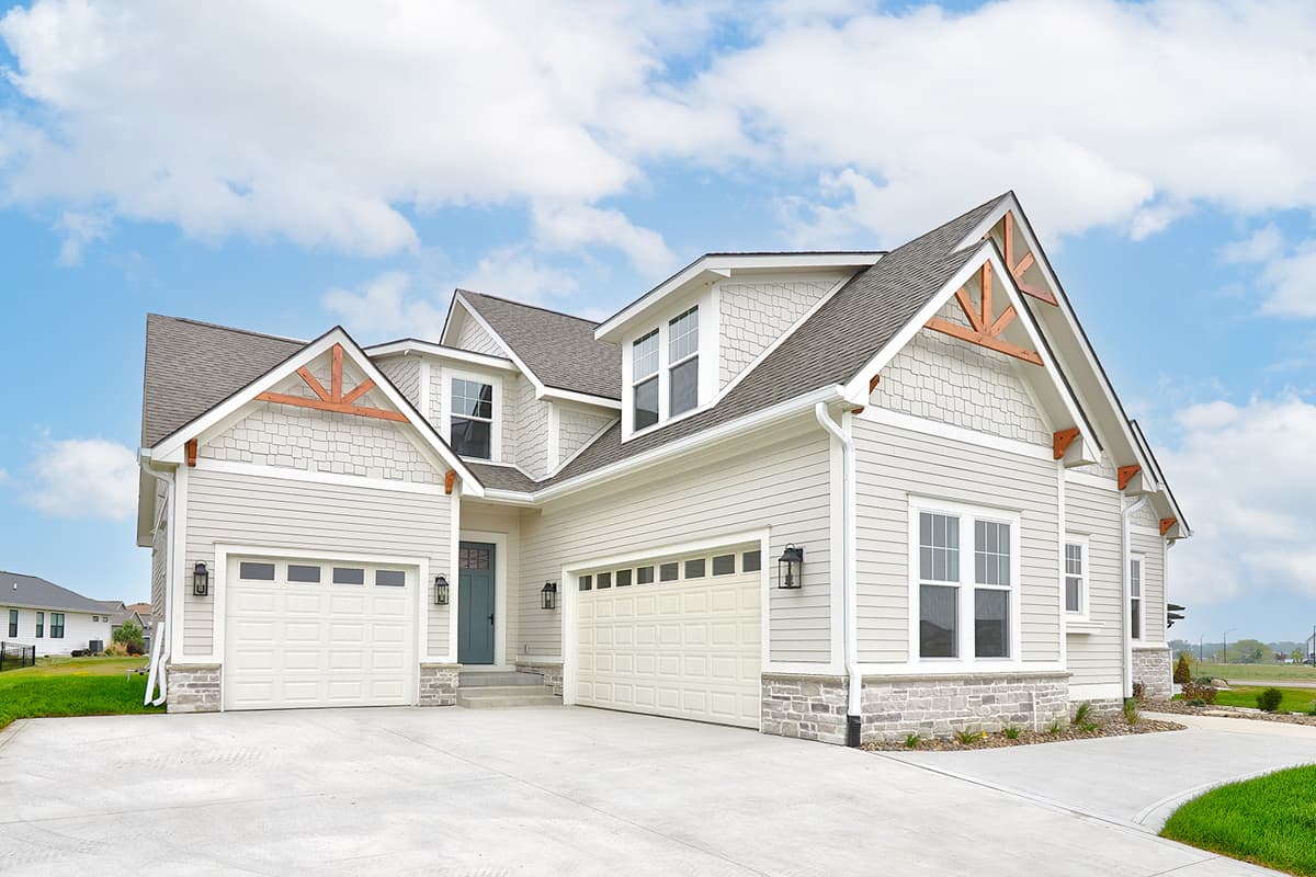 House plan exterior: Modern Farmhouse style, two stories, two garages, decorative gables with wood beams, and stone accents.