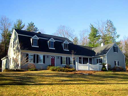 Two-story house plan exterior with gambrel roof, dormers, shutters, and a wraparound porch with white railing.