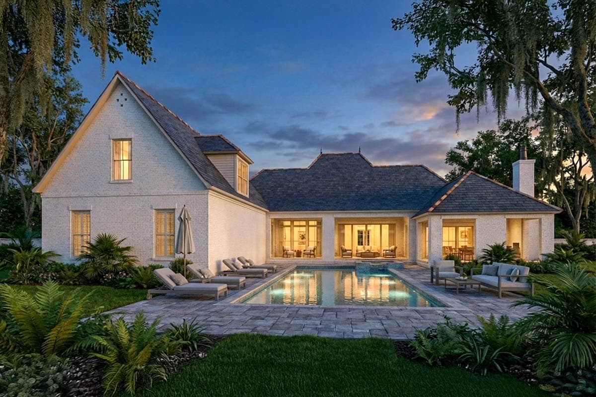 Exterior view of a luxury home at dusk, featuring a pool, patio, and lush landscaping. The house has a white brick facade and lit windows.