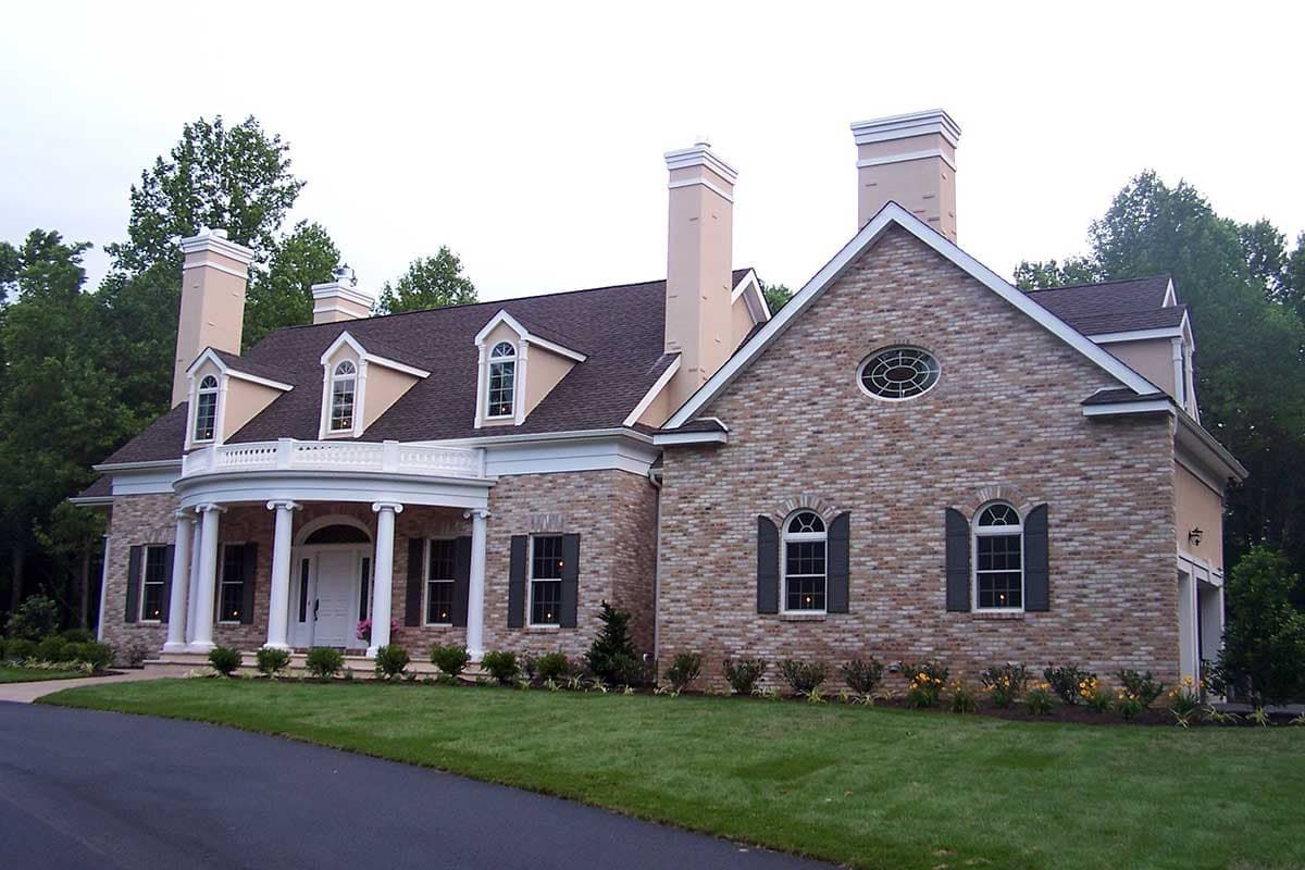 House plan exterior: Two-story brick home with a curved portico, white columns, dormers, and an oval attic window.