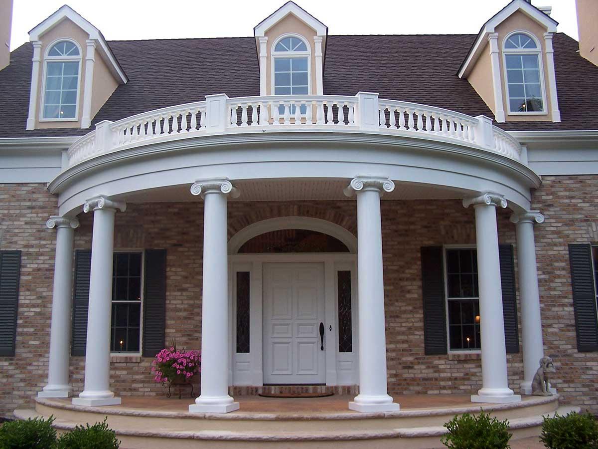 House plan exterior: two-story home with brick facade, curved portico supported by Ionic columns, and a second-story balcony.