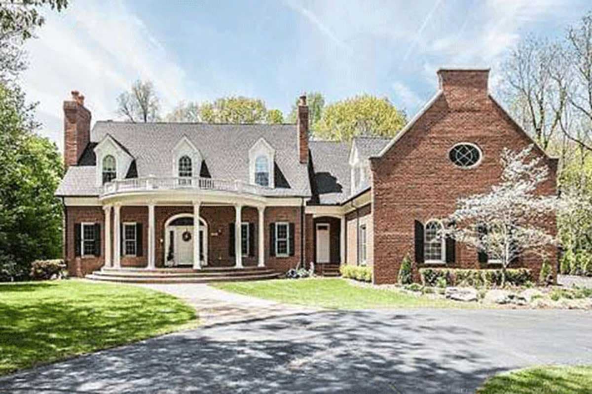 House plan exterior: two-story brick home with circular porch, multiple dormers, and prominent gabled section with oval window.