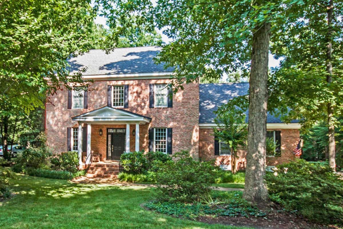 Brick two-story house plan with a covered front porch, symmetrical windows, and a steeply pitched roof.