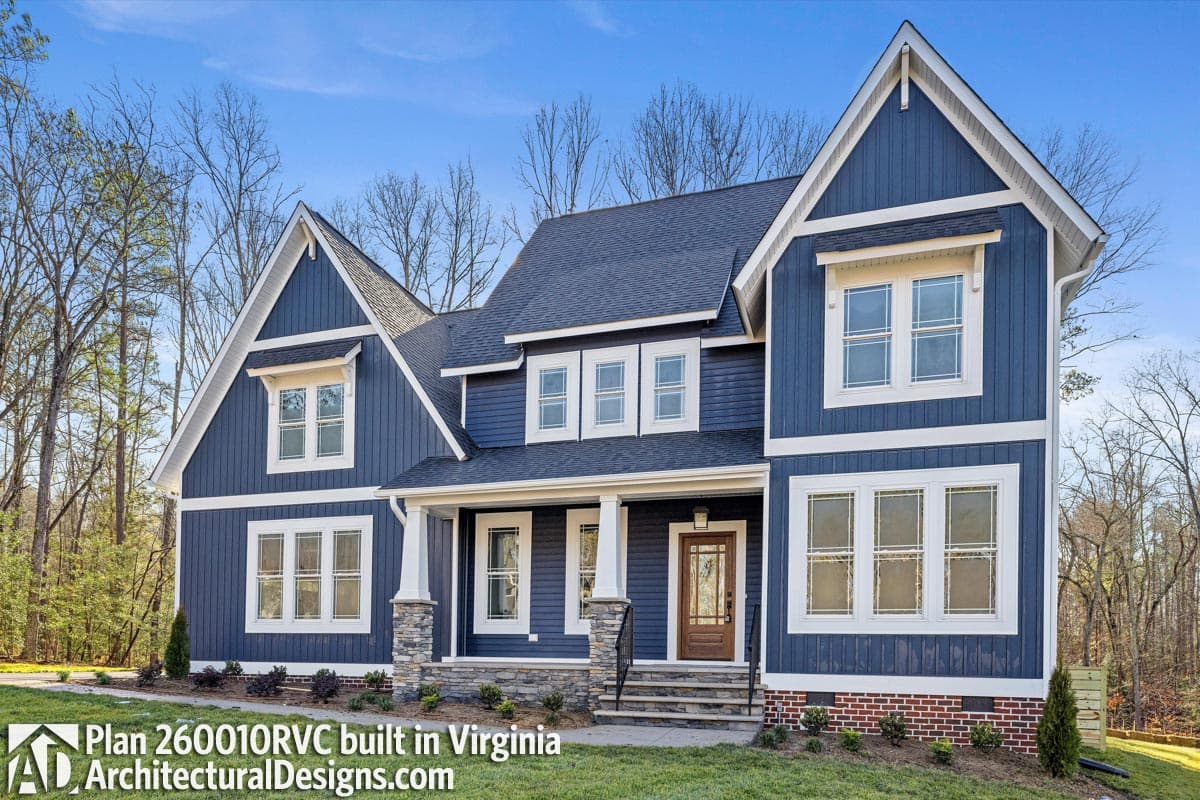 House plan exterior: blue siding, gabled dormers, stone porch supports, multiple stories, dark roof.