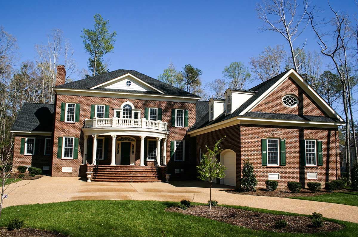 House plan exterior: Two-story brick home with a curved portico, second-story balcony, prominent gables, and attached garage.