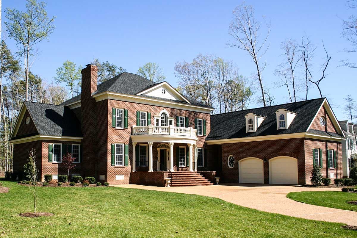 House plan exterior: Brick two-story home with a central portico, balcony, dormers, and attached three-car garage.