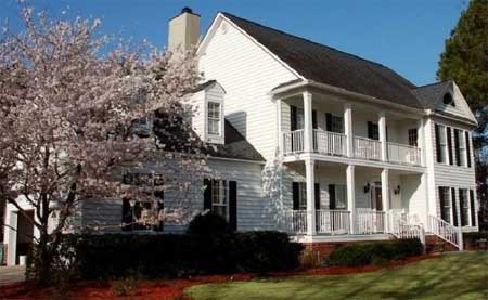 House plan exterior: two-story white home with double-tiered covered porches, gabled dormer, and multiple gables.