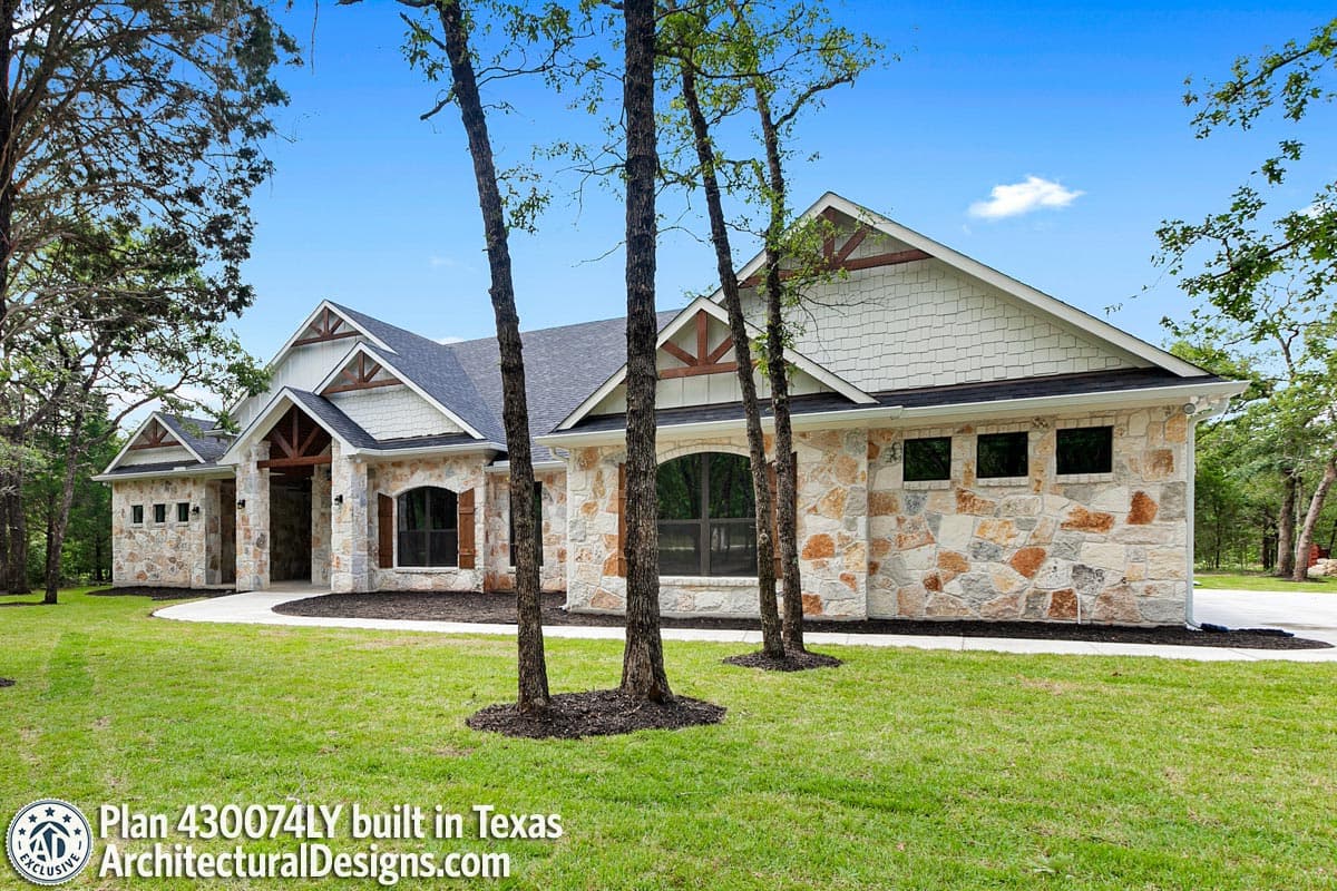 House plan exterior with stone veneer, gabled roof, and arched windows. Features exposed timber and shutters.