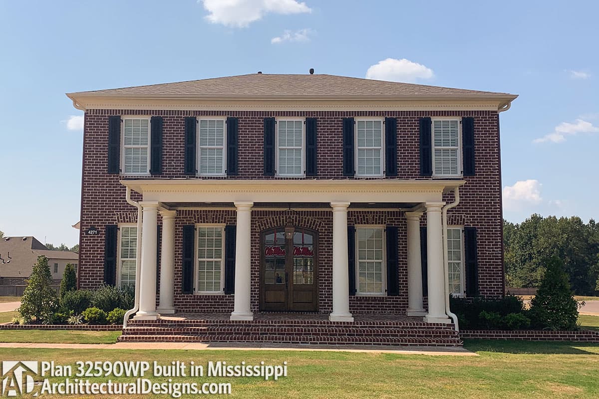 House plan exterior of a two-story brick home with a central portico supported by columns, shutters, and a pitched roof.