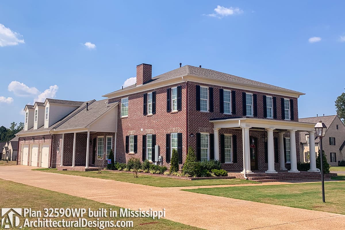 House plan exterior: Two-story brick home with a large portico, three dormers, and a three-car garage.