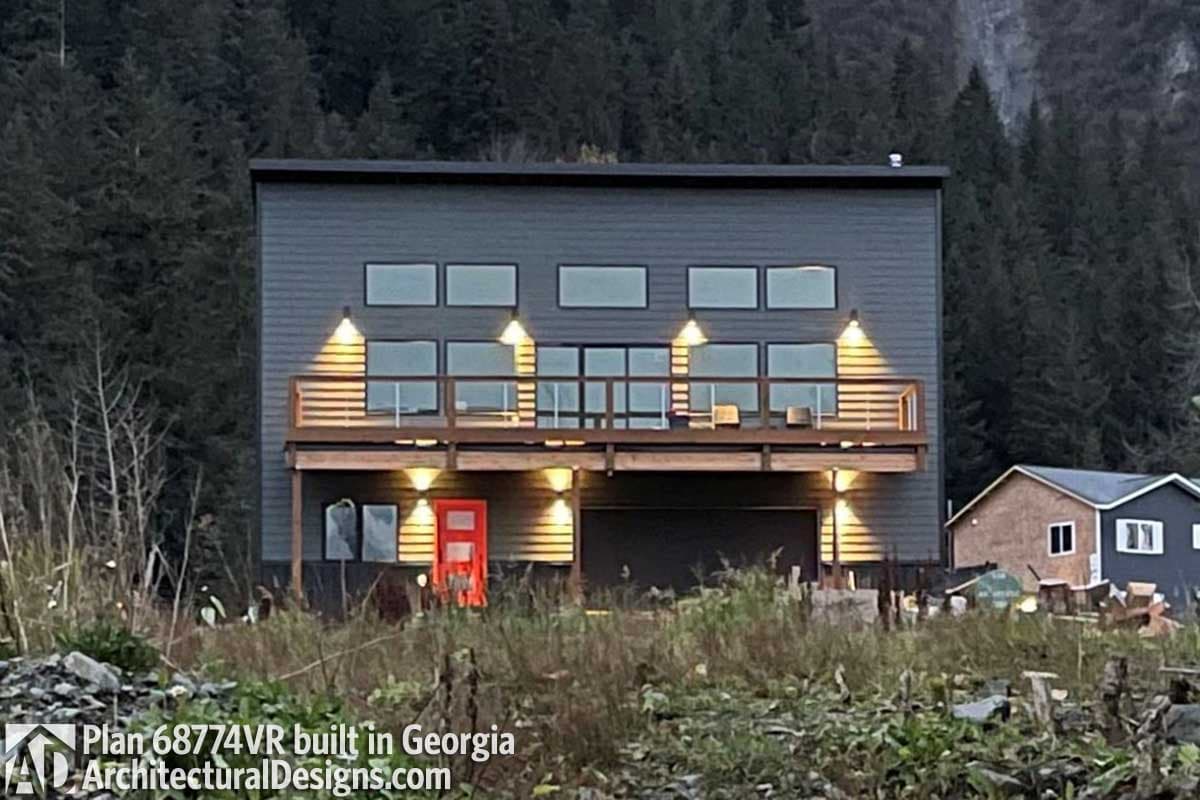 Modern two-story house plan exterior with horizontal siding, a cantilevered deck, large windows, and a red front door.