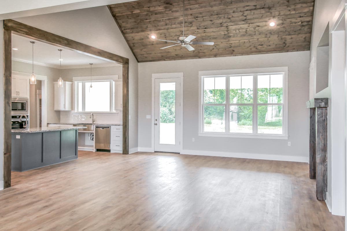 Open-concept living space with vaulted wood-plank ceiling, kitchen island, fireplace, and large windows.