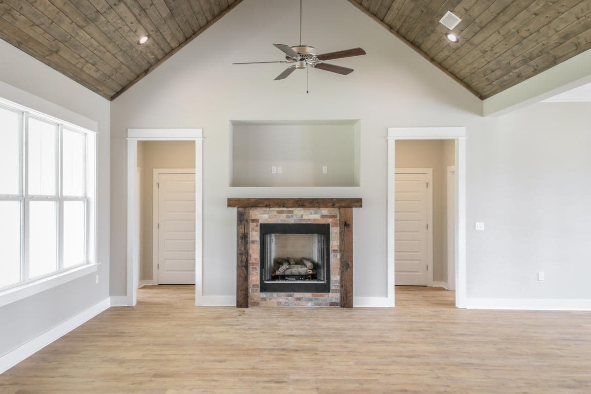 Interior view of living room with vaulted wood-paneled ceiling, fireplace, and two doorways.