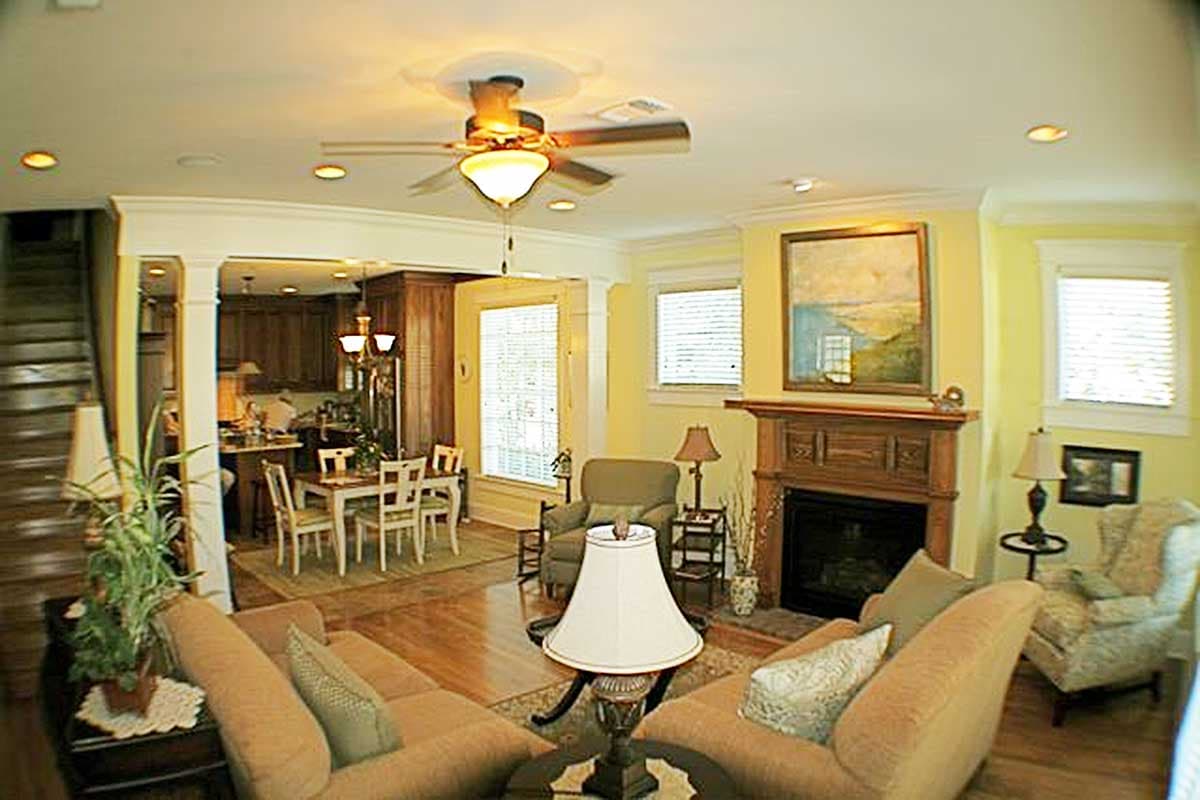 Interior view of a living room with a fireplace, dining area, and kitchen visible. Features include wood floors, a ceiling fan, and recessed lighting.