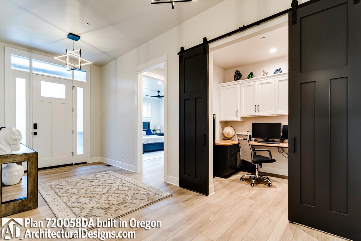 Interior view of house entrance with doorway to bedroom and office featuring barn door, desk, and built-in cabinets.