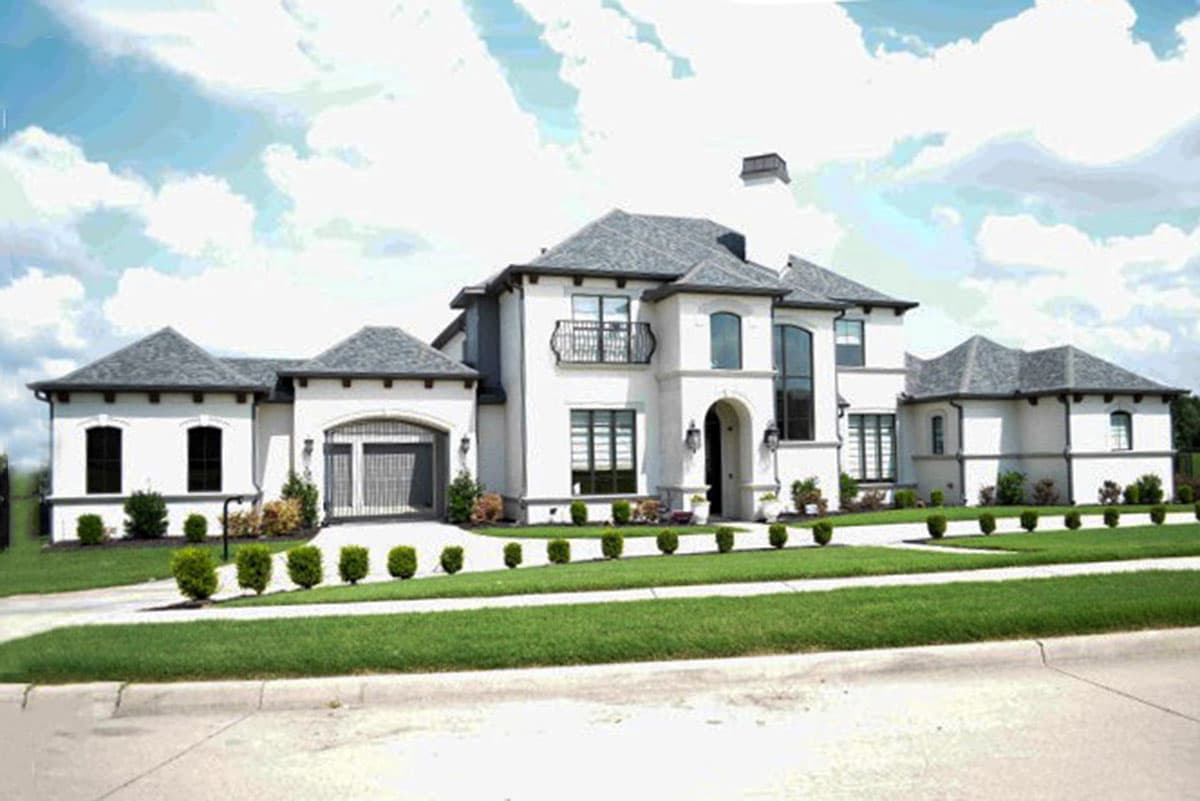 House plan exterior: Two-story white stucco residence with multiple gables, arched entryway, and attached garage.