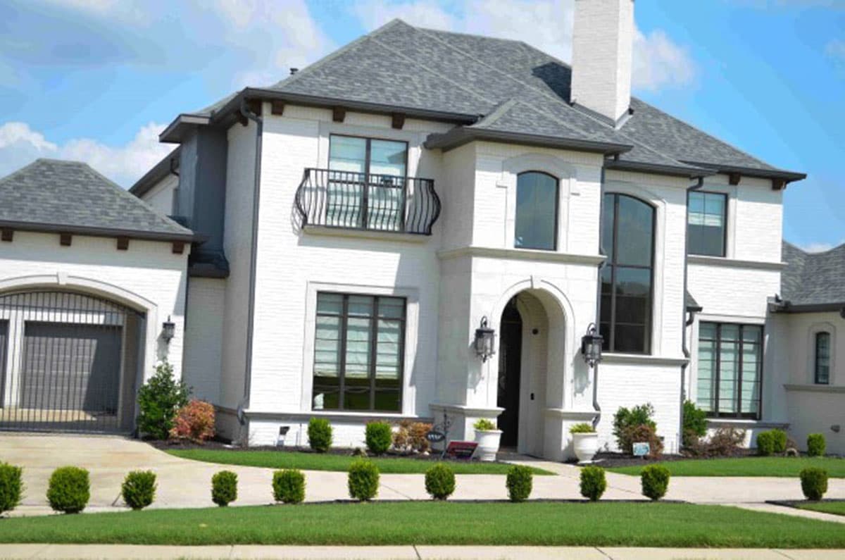 House plan exterior: Two-story modern home with arched entryway, balcony, white brick facade, and attached garage.