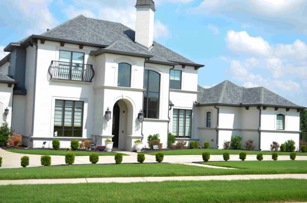 House plan exterior: Two-story stucco home with arched entry, balcony, prominent chimney, and multiple gables.
