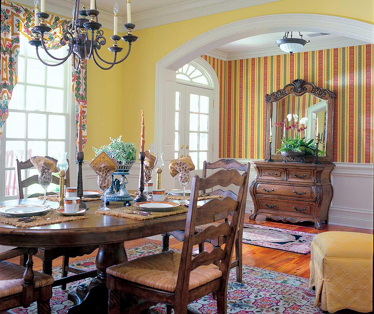Dining room with oval table set for four, arched entryway with double doors, and striped wallpaper accent wall.