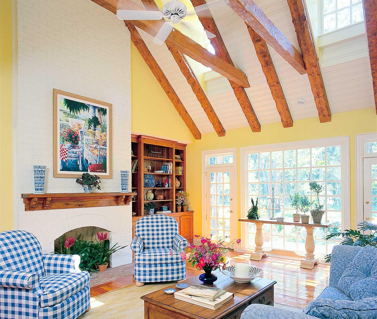 Living room with vaulted ceiling, exposed wood beams, brick fireplace, built-in bookshelves, and large windows.