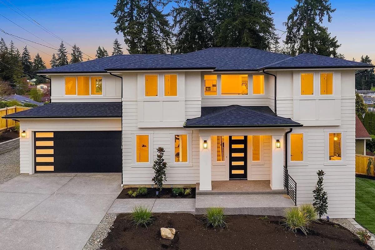 House plan exterior: Two-story contemporary home with black roof. Features include a garage, porch, and multiple windows with warm lighting.