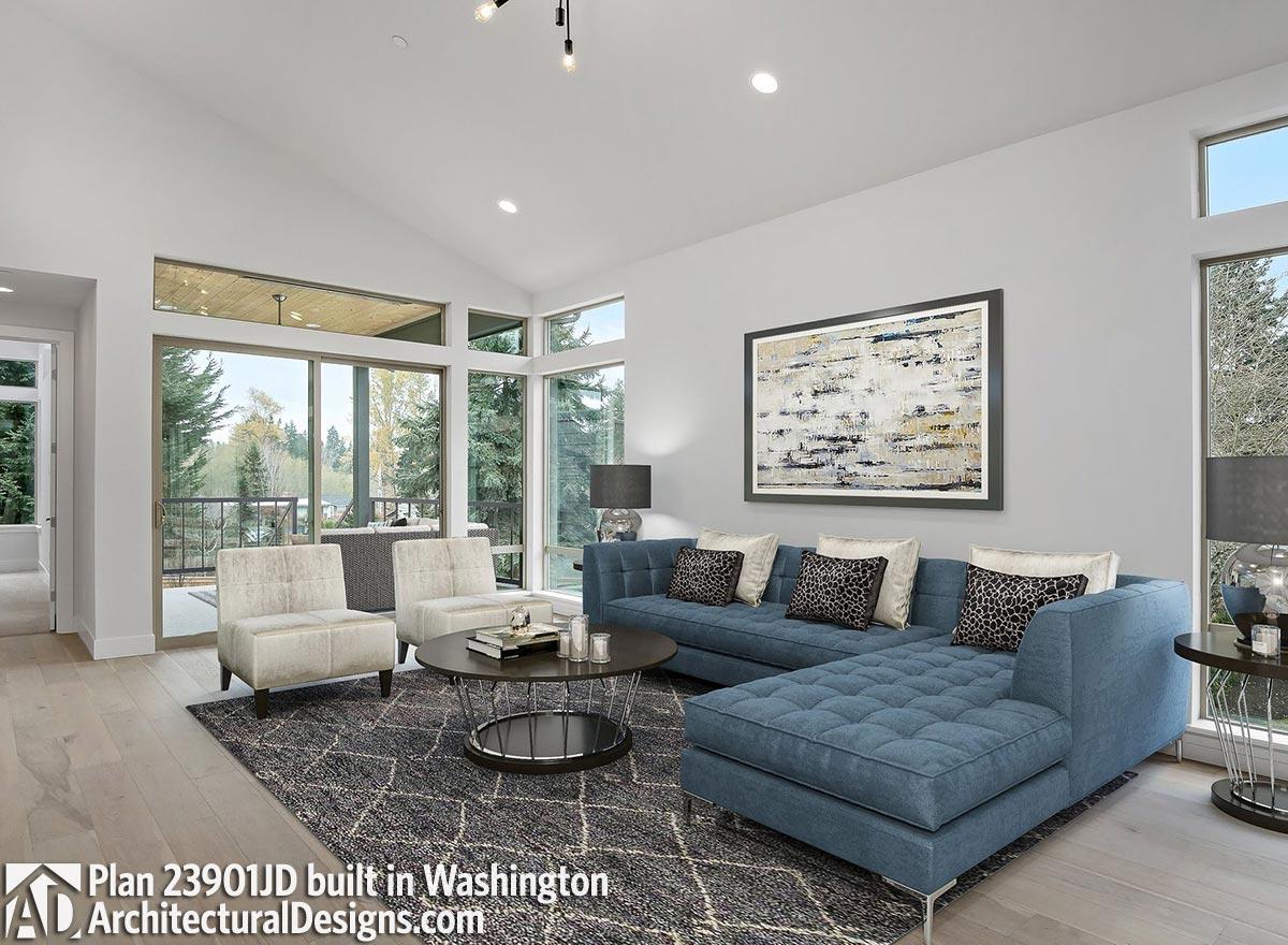 Living room with vaulted ceiling, large windows, blue sectional sofa, and access to covered patio. Plan 23901JD.