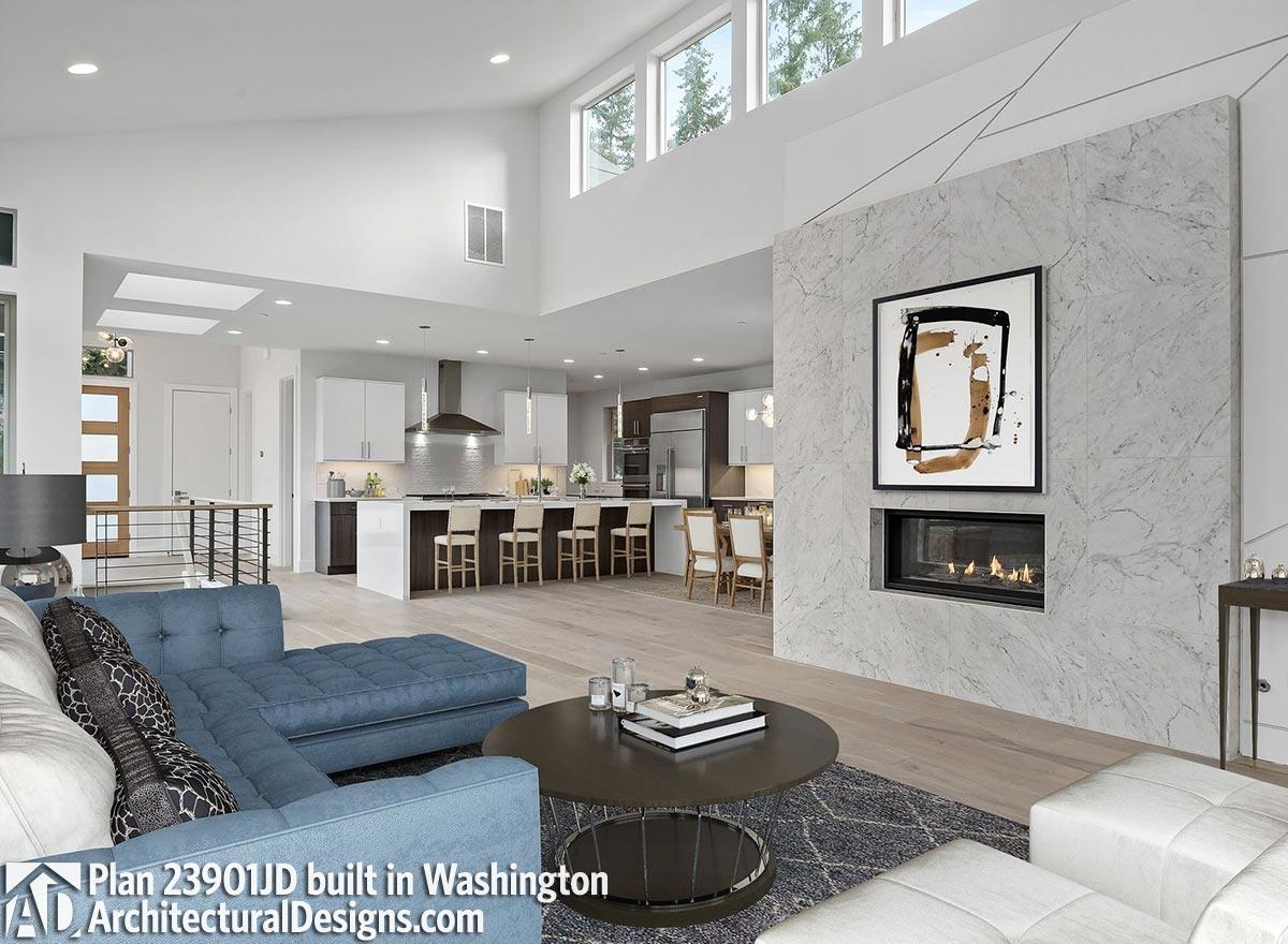 Open concept living area with vaulted ceiling, modern fireplace, kitchen island with seating, and large windows.
