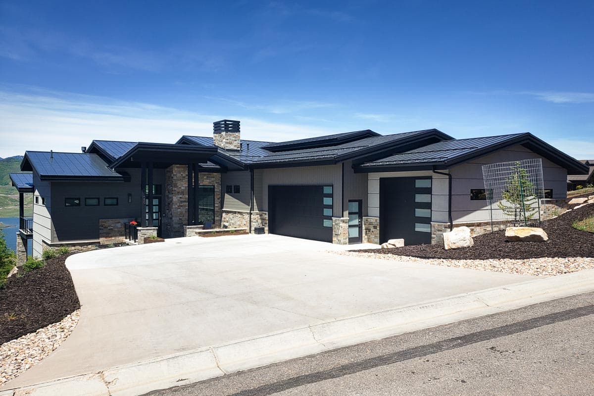 Modern house plan exterior with low-slope rooflines, stone facade accents, and a two-car garage. Features a covered entry and a concrete driveway.