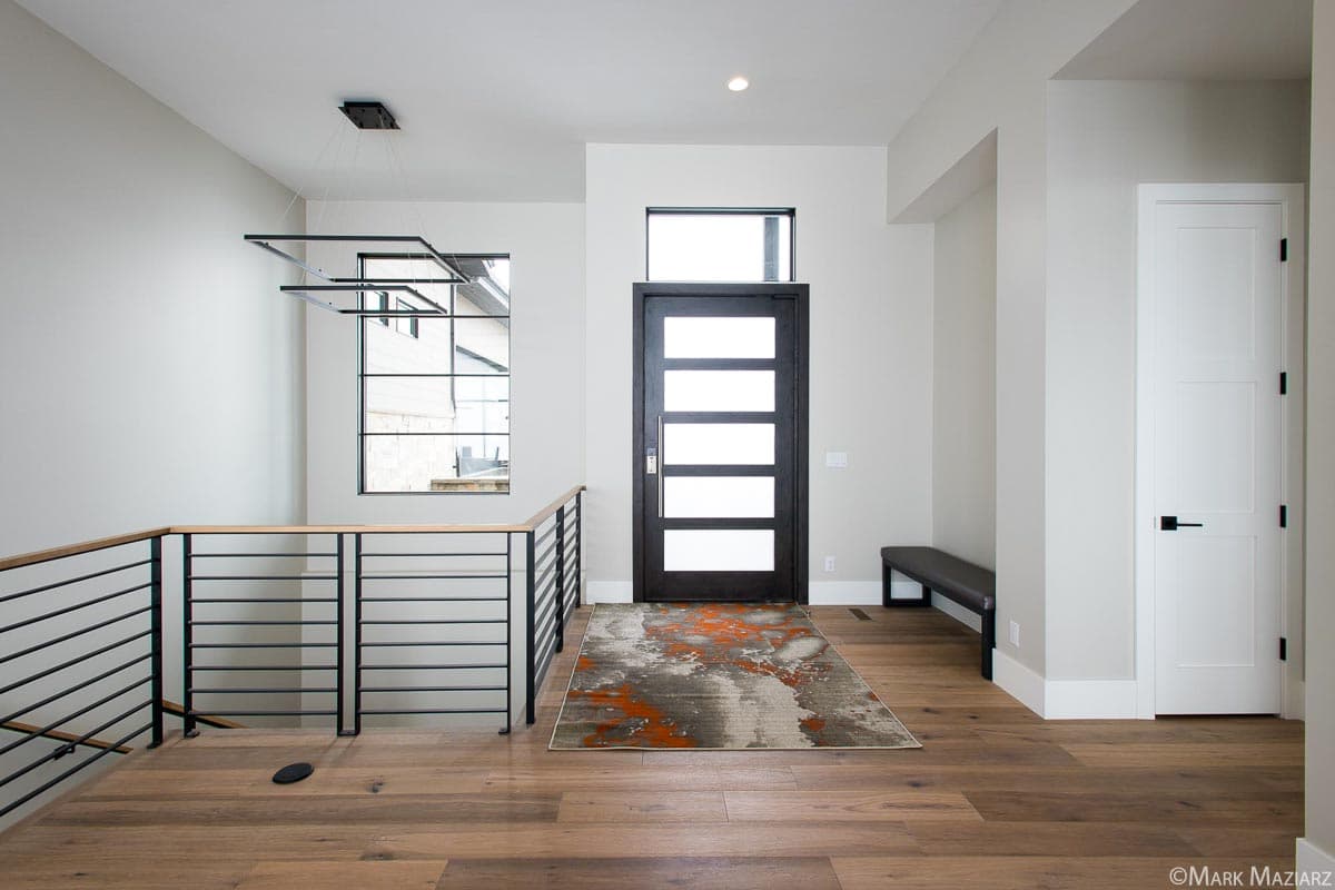 Interior view of modern foyer with horizontal paneled door, railing, and geometric chandelier.