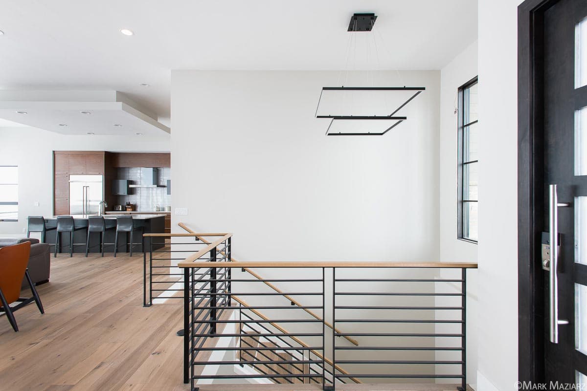 Modern interior view with open staircase, wood floors, and contemporary kitchen in background.