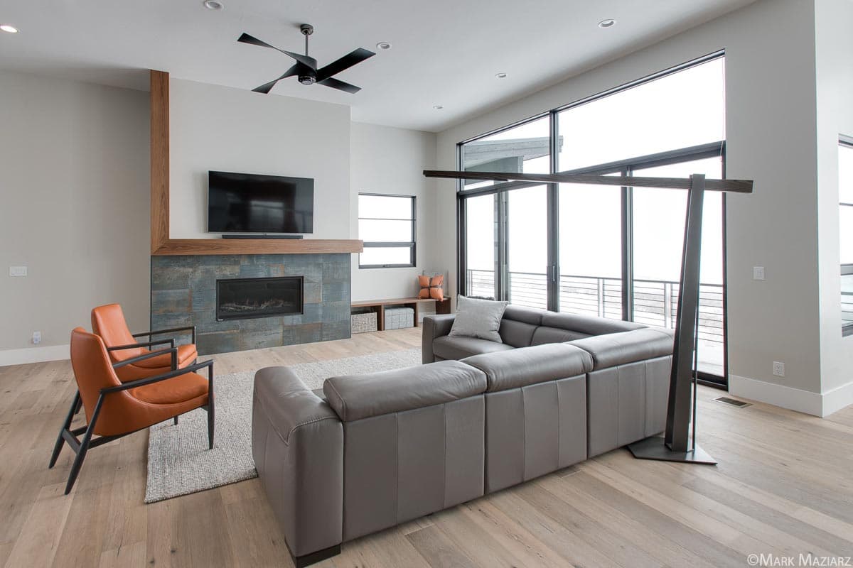 Interior view of a great room with a fireplace, sectional sofa, and large windows.