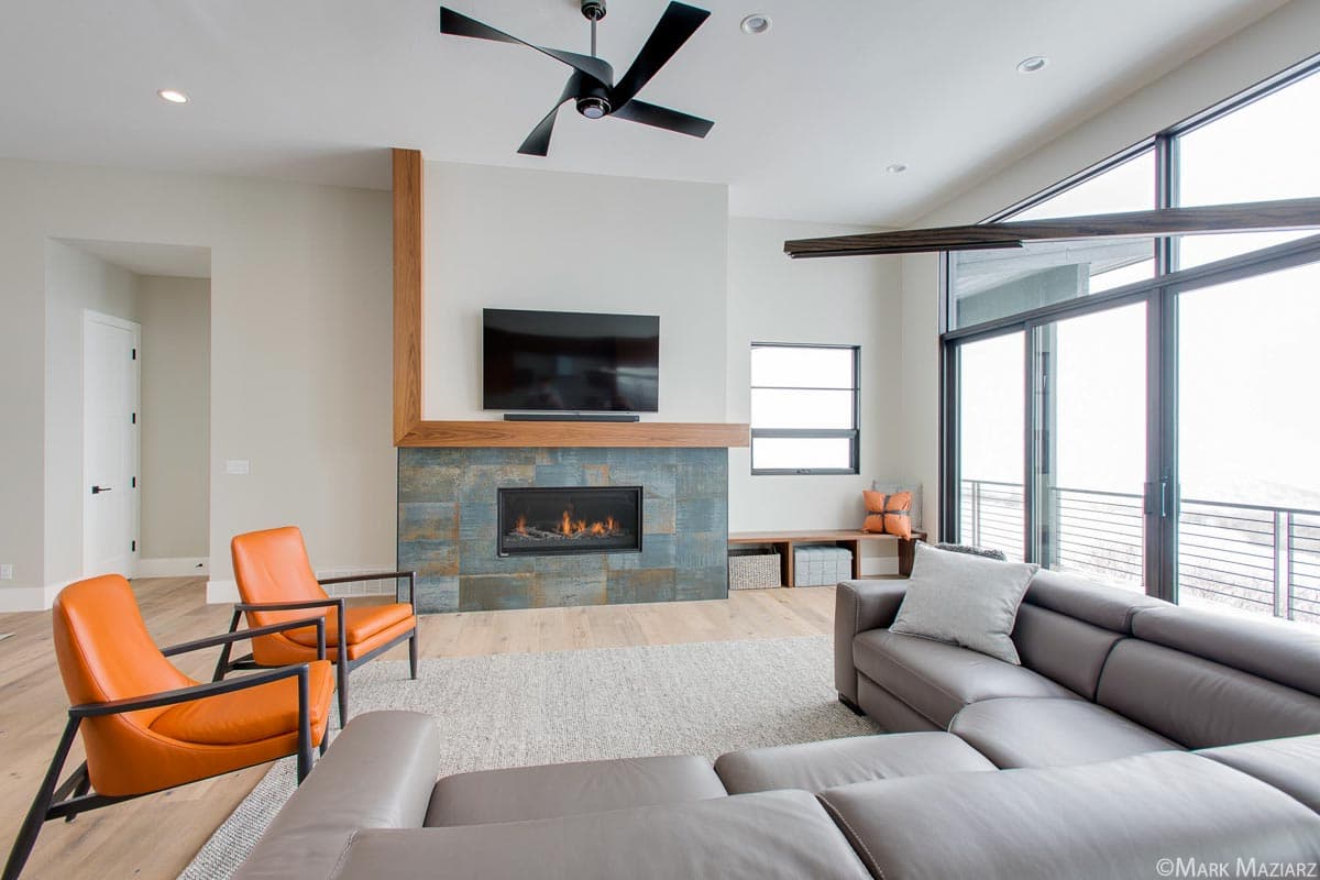 Modern living room with fireplace, large windows, contemporary ceiling fan, and sectional sofa.