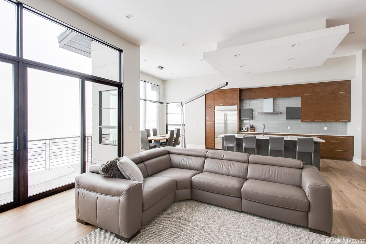 Open concept living area with a sectional sofa, island kitchen featuring wood cabinetry, and large windows.