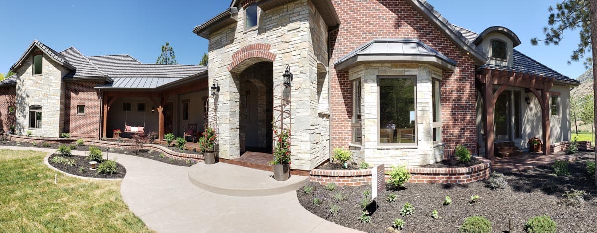 House plan exterior features stone and brick facade, arched entryway, covered porch with swing, and bay window.