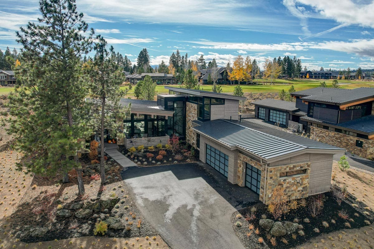 Modern house plan exterior with stacked stone accents, metal roof, and multi-car garage with glass panel doors.