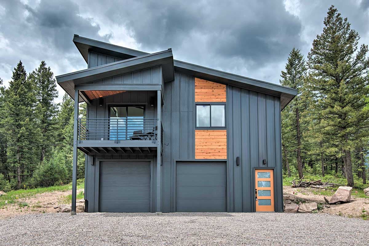 House plan exterior. Modern style, two-story home with a sloped roof, balcony, and two-car garage. Features wood accents and a modern entry door.