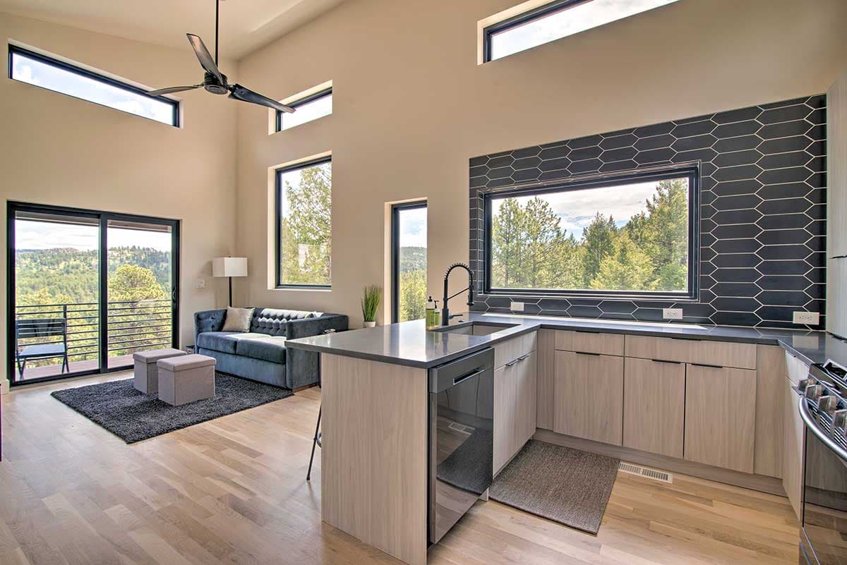 Modern living area and kitchen with vaulted ceiling, large windows, island with sink, and sectional sofa.