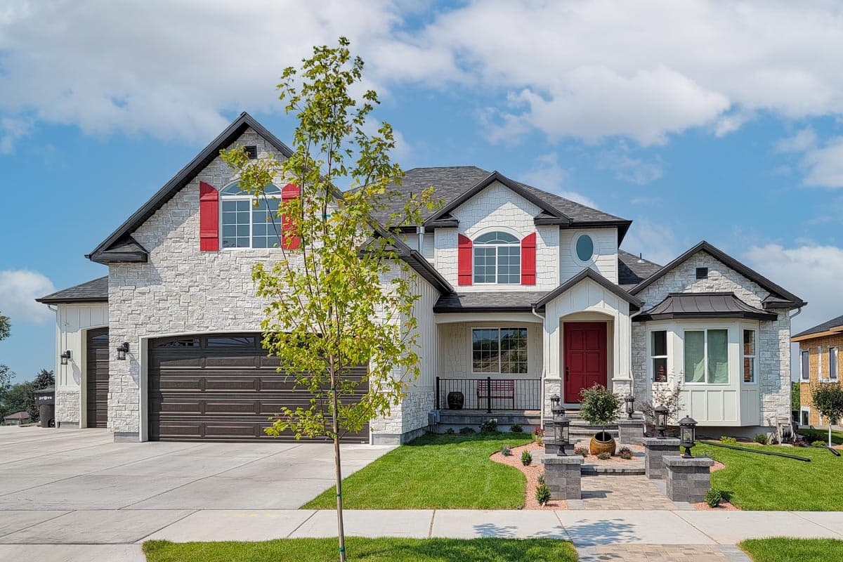 House plan exterior with stone veneer, gabled roof, and red shutters. Features include a front porch and a three-car garage.