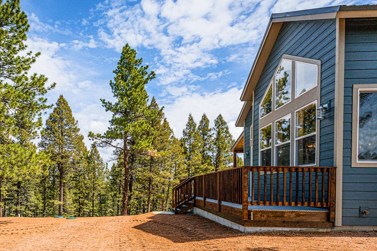 House plan exterior with dark blue siding, large triangular and rectangular windows, and a wooden deck.