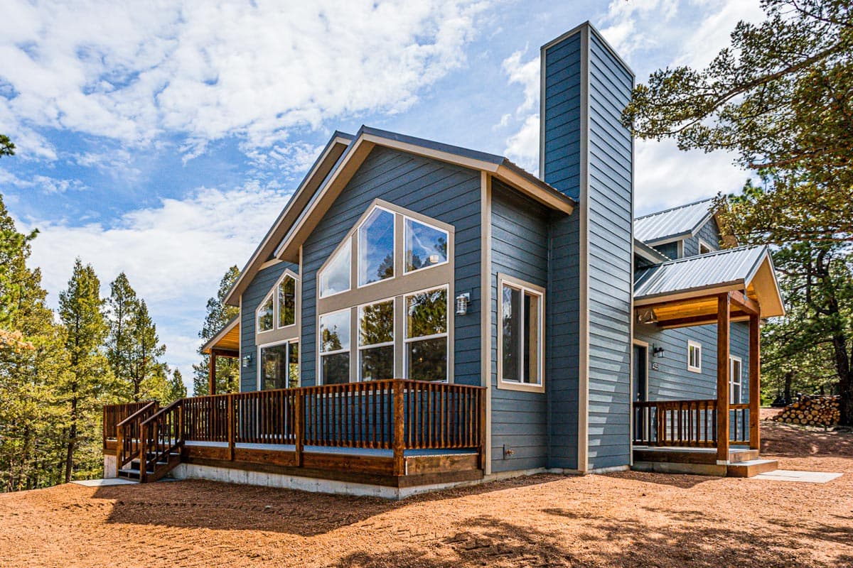 House plan exterior: Two-story home with large deck, prominent chimney, and expansive gable-end windows.