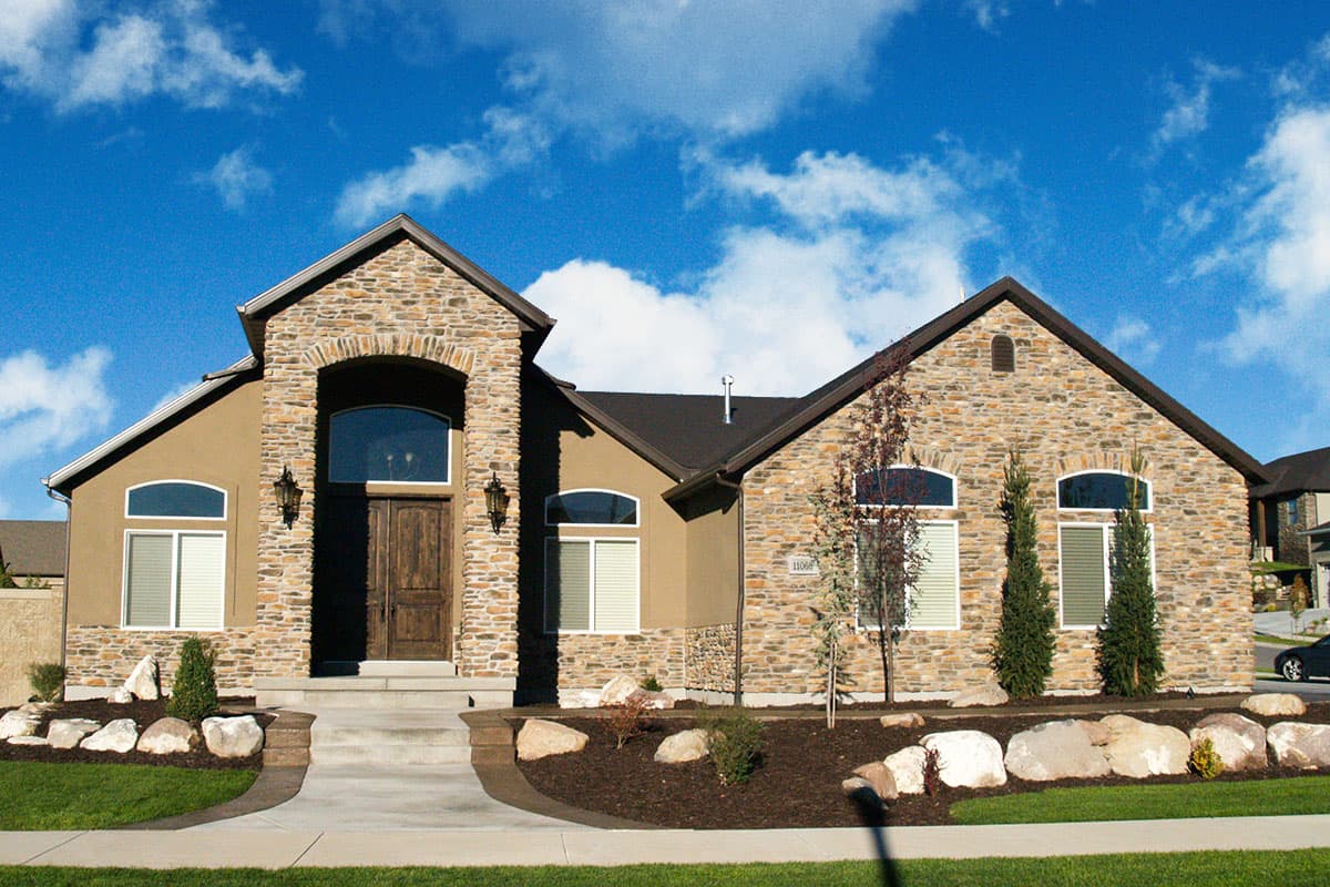 House plan exterior. Two-story home with stone facade, arched entryway, and multiple gables. Features include dormers and a prominent roofline.