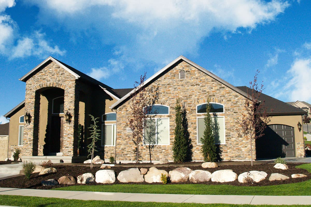 House plan exterior: Two-story home with stone facade, arched entry, gabled roofs, and attached garage.